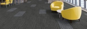 Studio shot of the front guest area, using Outfitter carpeting. Two yellow cushioned chairs surround a small round coffee table.